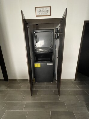 A compact laundry room with a washing machine and dryer, a sign above indicating it's a laundry room, and a tiled floor.