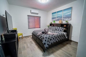 Een slaapkamer met een bed, een bureau, een stoel, een airconditioner en een raam met jaloezieën.