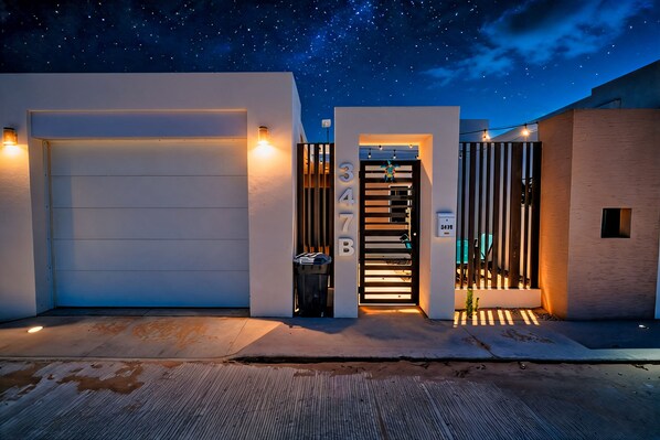 A modern residential building with a garage, a gated entrance, and a starry night sky.