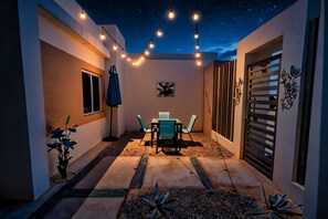 An outdoor patio area with a table and chairs, string lights, and decorative plants.