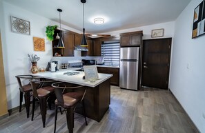 A modern kitchen with a central island, bar stools, stainless steel appliances, and a hanging plant.