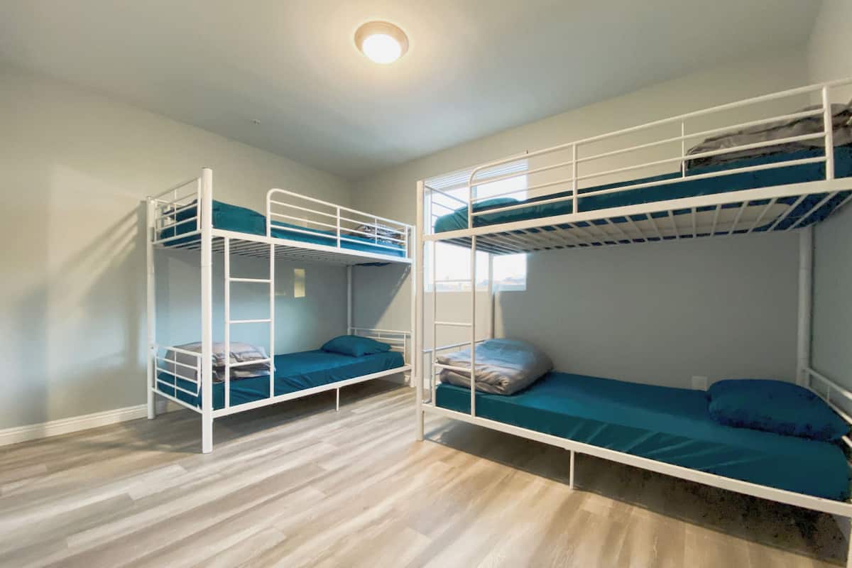 A room with two bunk beds, wooden flooring, and a window providing natural light.