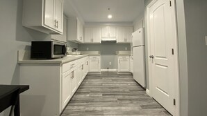 A narrow kitchen with white cabinets, a microwave, and a refrigerator. - Modern Hostel (Los Angeles)