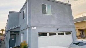 A two-story residential building with a garage door, a small window, and a visible address sign. - Modern Hostel (Los Angeles)
