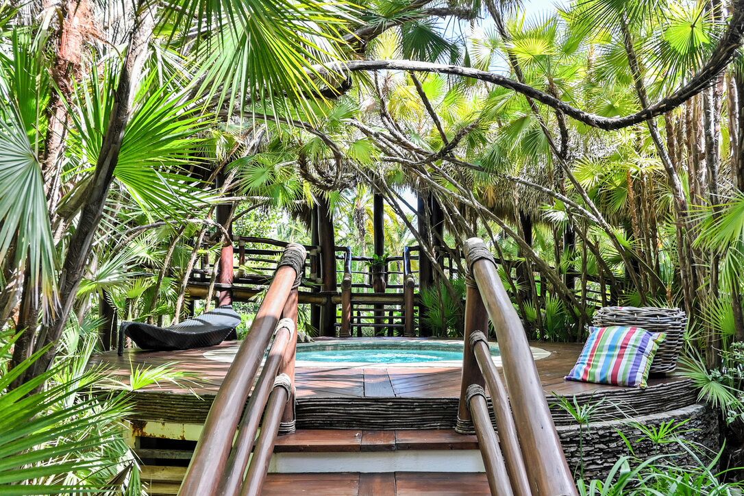 A wooden deck with a hot tub, surrounded by lush tropical foliage.