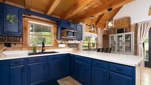 A modern kitchen with blue cabinets, a white countertop, and a wooden ceiling.