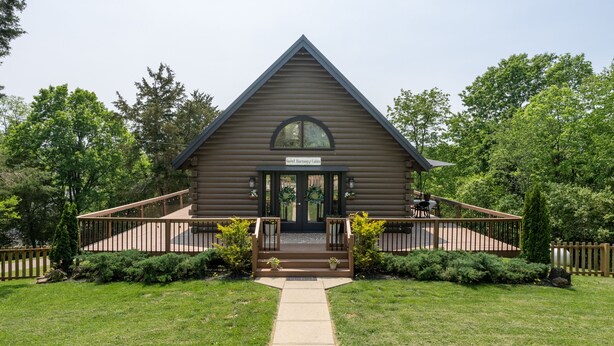 A log cabin with a front porch, a small deck, and a sign that reads "Sweet Harmony Cabin".