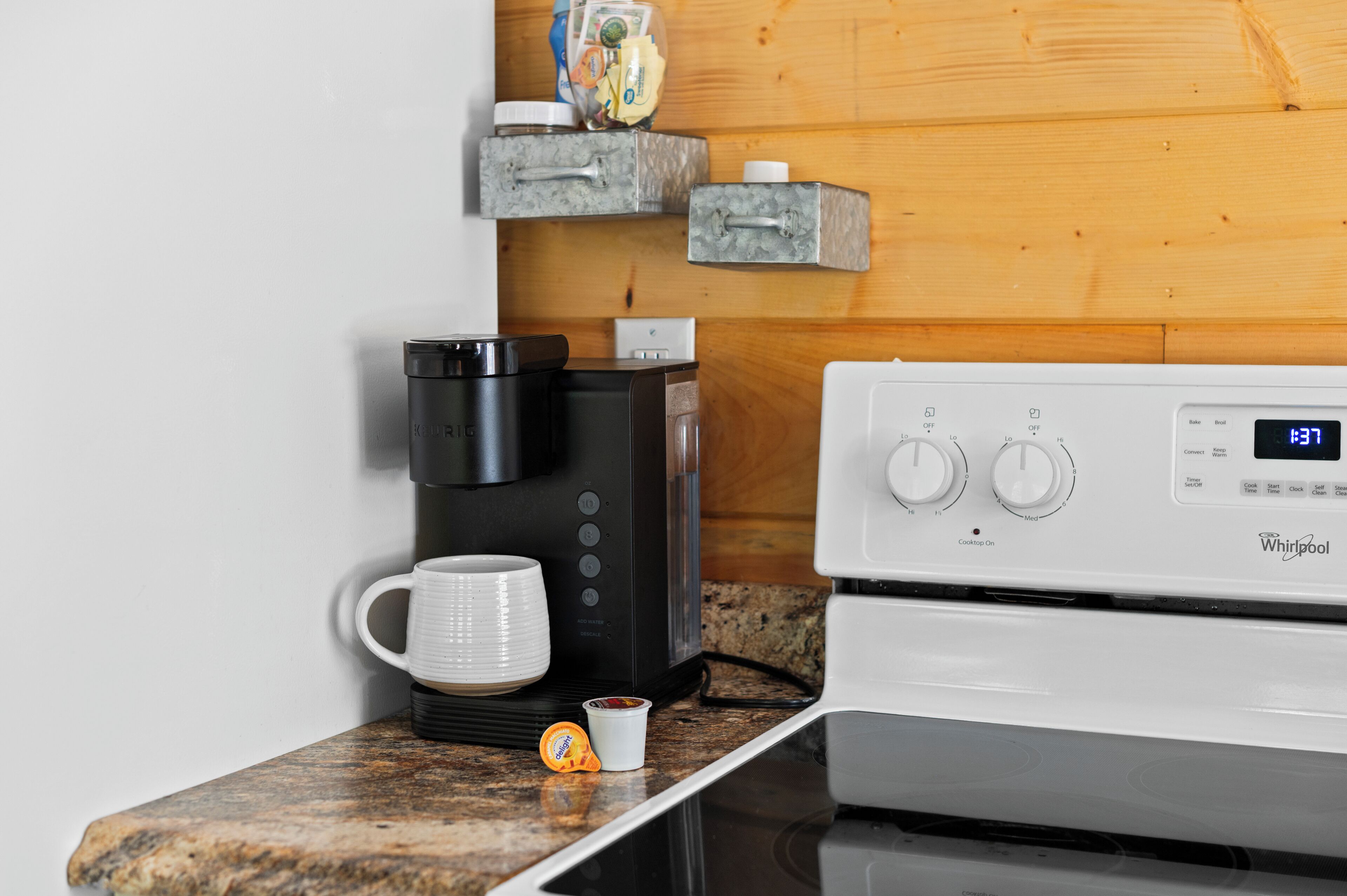 A kitchen with a coffee maker, a white mug, and a digital clock displaying 1:37.