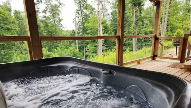 Ein Whirlpool mit einer Holzterrasse und Blick auf einen Wald.