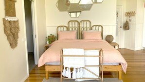 Um quarto com cama, cabeceira, espelho, mesa de cabeceira e planta pendurada.
