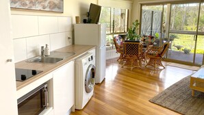Uma cozinha moderna com máquina de lavar e secar embutidas, área de jantar com cadeiras de vime e amplas janelas com vista para o exterior.