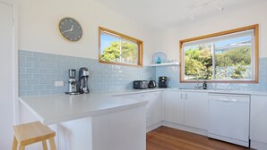 A modern kitchen with white cabinets, a wooden stool, a coffee maker, and a dishwasher.