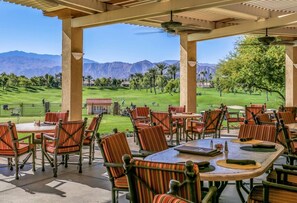 Eine Terrasse im Freien mit Tischen und Stühlen mit Blick auf einen Golfplatz und Berge.