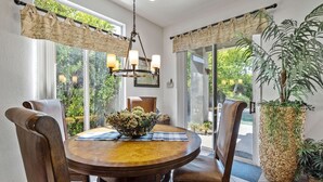 A dining area with a round table, chairs, a chandelier, and a large potted plant. - Casa Royal Troon- Active 55+ Golf Course Community, Private Home w Pool and Spa! (Indio)