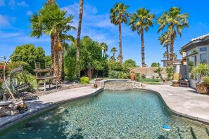 Ein Pool mit klarem Wasser, umgeben von Palmen und einer Steinstruktur.