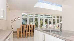 A modern kitchen with a skylight, large windows, and a dining area with wooden chairs.