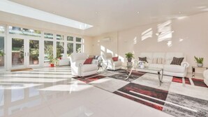 A spacious living room with a large glass door leading to a garden, white sofas, and a coffee table.