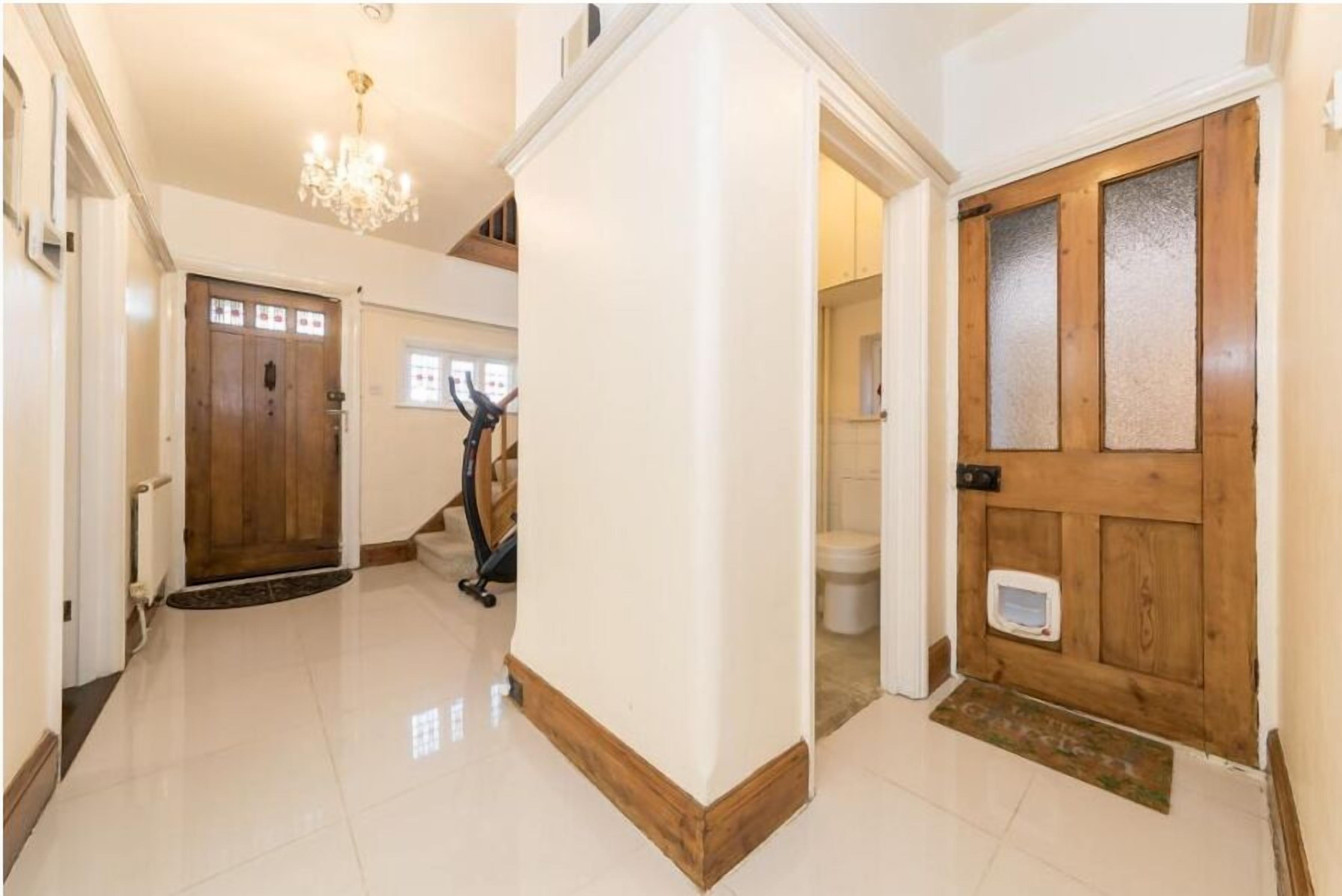 A hallway with a wooden door, a white wall, and a chandelier.