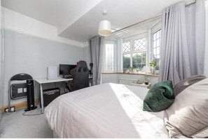 Une chambre d’hôtel avec un lit, un bureau, une chaise et une fenêtre avec des rideaux.