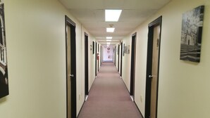 Un long couloir étroit, avec des portes de chaque côté, un sol recouvert de moquette et des murs de couleur claire.