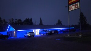 Un motel dont l’extérieur est illuminé de lumière bleue et qui affiche une enseigne indiquant qu’il s’agit du « Midway Motel ».