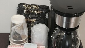 Un plateau contenant une cafetière, des sachets de thé, une carafe en verre et un sachet de sucre.