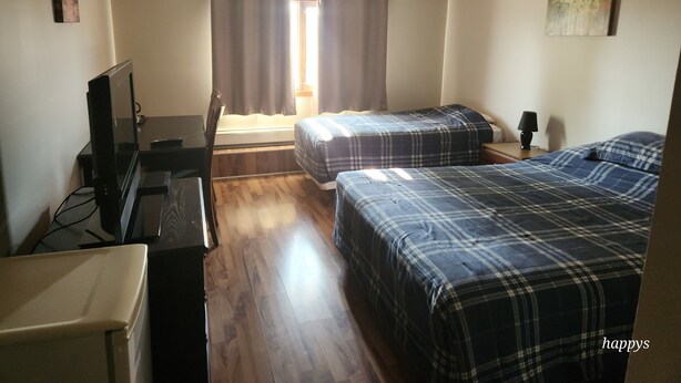 Une chambre avec deux lits, un ventilateur de plafond, un bureau et un téléviseur.