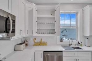 A modern kitchen with white cabinetry, a built-in microwave, a toaster, and a window with a view of the ocean.
