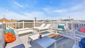 Eine Dachterrasse mit weißen Geländern, Liegestühlen und bunten Kissen.