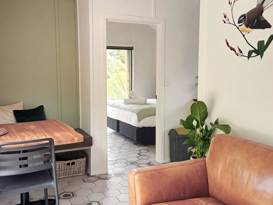 A room with a wooden dining table, a grey chair, a brown leather sofa, and a large green plant.