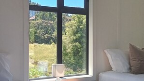 Quarto com uma janela grande, mesa de cabeceira com abajur e duas camas.