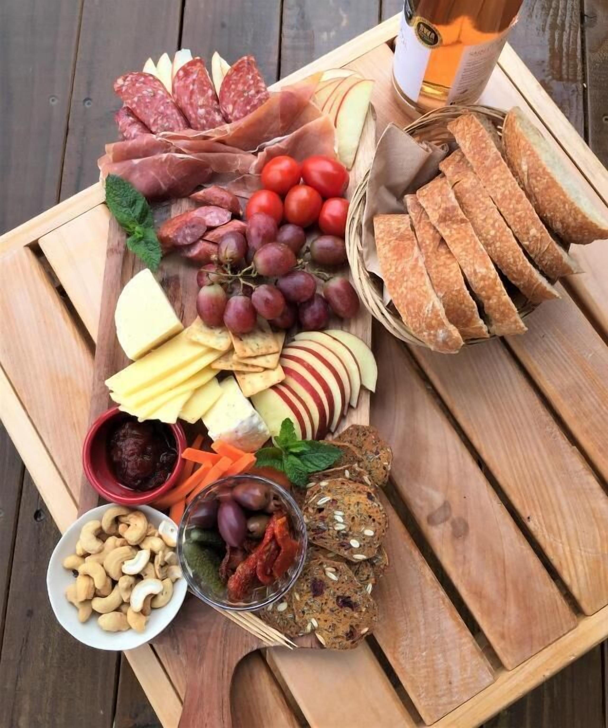 Une table en bois sur laquelle est disposée une planche de charcuterie, avec une variété de viandes, de fromages, de fruits, de noix et de pain.