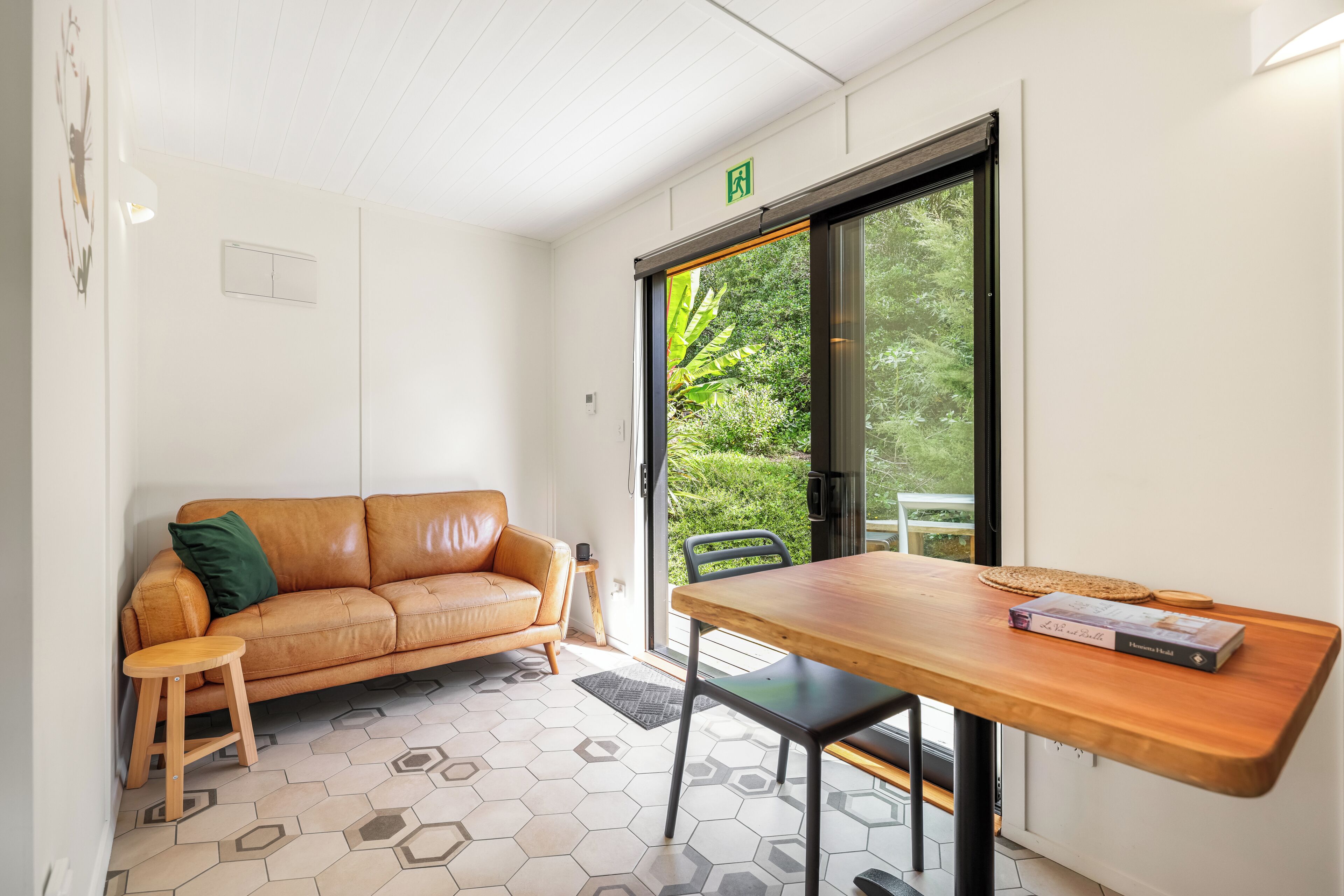 Quarto moderno com sofá de couro, mesa de madeira e uma janela grande com vista para área verde.