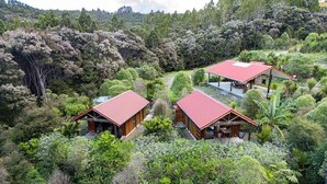 Uma pousada isolada com três cabanas rodeadas por uma floresta densa, cada uma com telhado vermelho e construção em madeira.