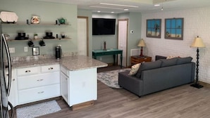 A spacious living area with a kitchen, a gray sofa, a dining table, and a ceiling fan. - Courtyard Bungalow
 (Melbourne)