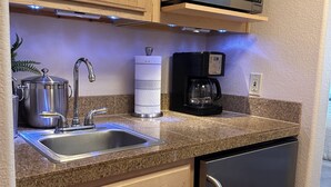 Una cocina compacta con refrigerador de acero inoxidable, microondas, cafetera y lavamanos con grifo.