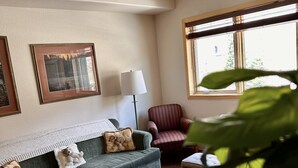 Una sala de estar con un sofá verde, un sillón a rayas, una lámpara y cuadros en la pared.