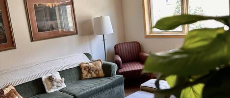 Una sala de estar con un sofá verde, un sillón a rayas, una lámpara y cuadros en la pared.