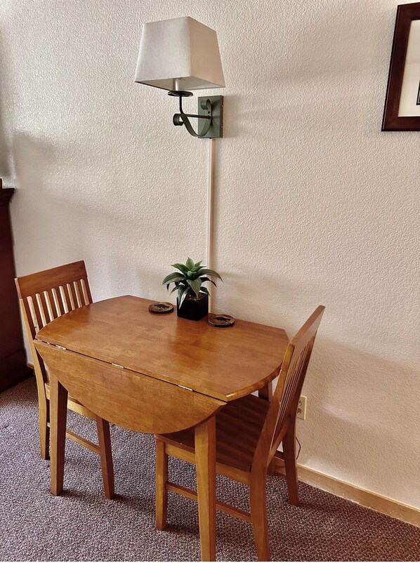 A wooden dining table with four chairs, a potted plant, and a wall-mounted lamp.
