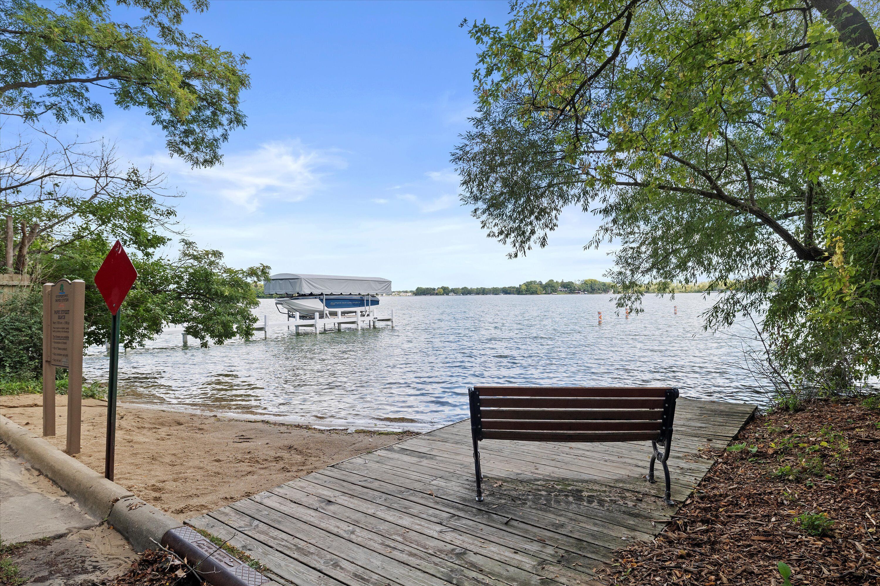 Une jetée en bois avec un banc, un bateau amarré à l’eau et un panneau indicateur.