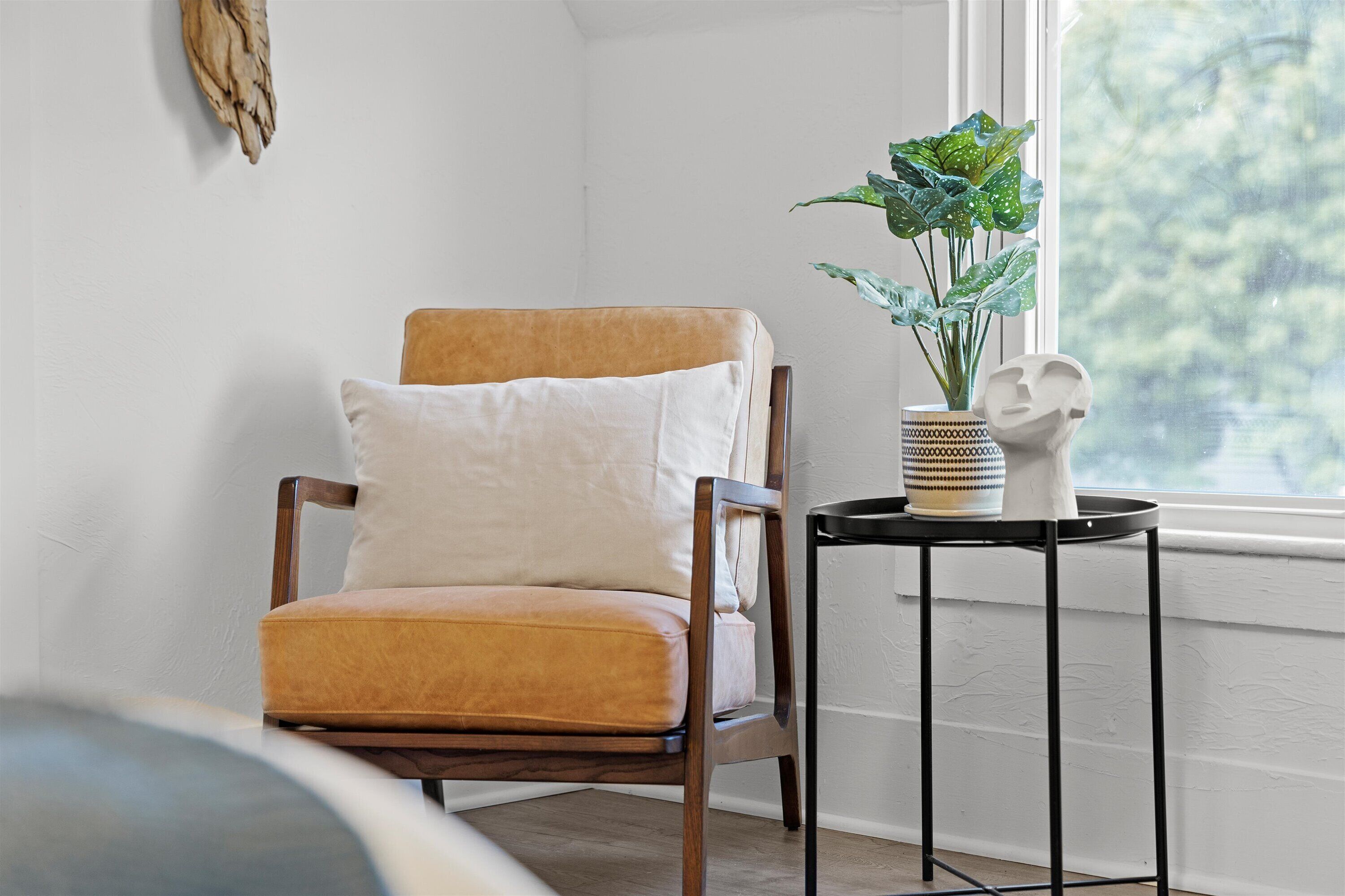 Een hoek van een kamer met een houten stoel, een witte kussen, een klein tafeltje met een plant en een decoratieve vaas.