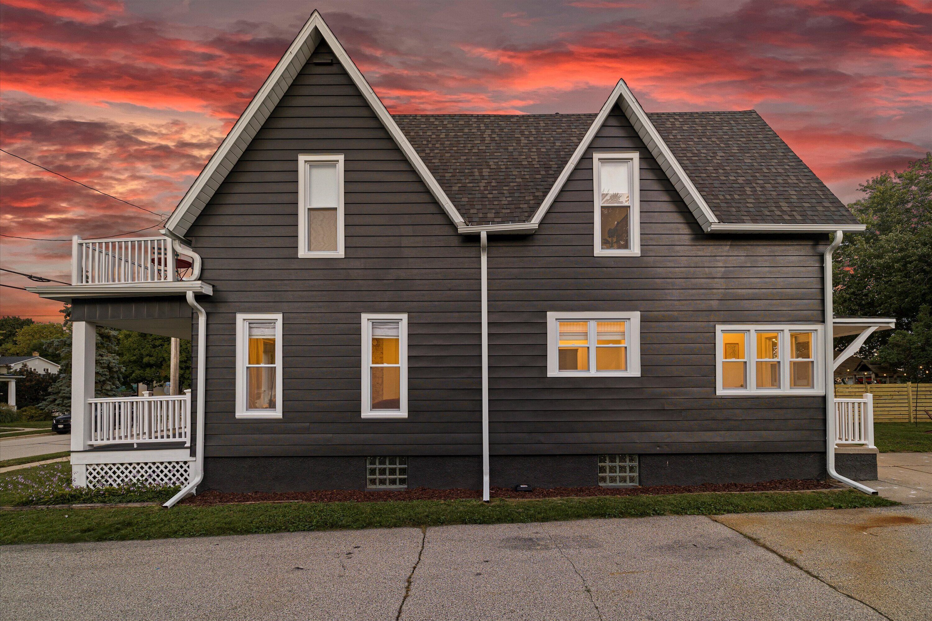A two-story house with a dark exterior, white trim, and a small porch with a railing.