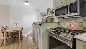 Een keuken met een houten eettafel, stoelen, een fornuis, een magnetron en een waterkoker.
