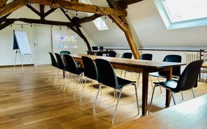 Een vergaderruimte met een houten tafel, zwarte stoelen, een whiteboard en een projectiescherm.