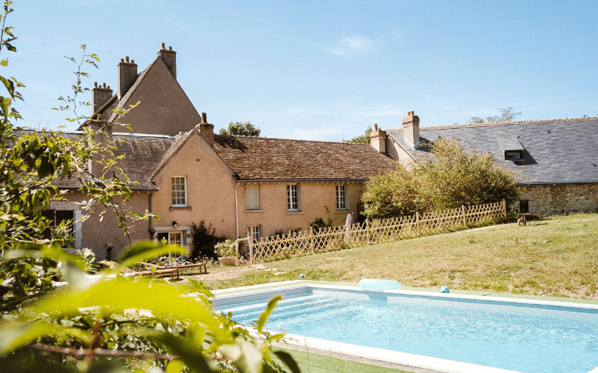 A traditional house with a swimming pool, surrounded by a wooden fence and greenery.