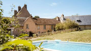 A traditional house with a swimming pool, surrounded by a wooden fence and greenery.