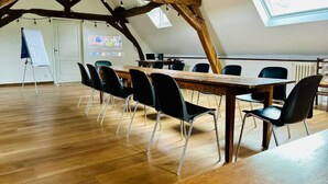 Un salón de conferencias con una mesa de madera, sillas negras, una pizarra y una pantalla de proyector.