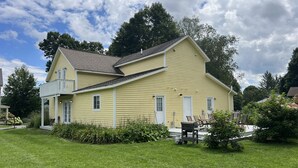 A two-story yellow house with a balcony, surrounded by a well-maintained lawn and trees.