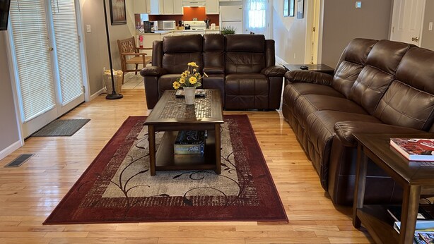 A living room with a brown leather sofa, a coffee table with a vase of flowers, and a wooden floor.