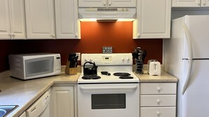A kitchen with white cabinets, a stove, a microwave, and a refrigerator.